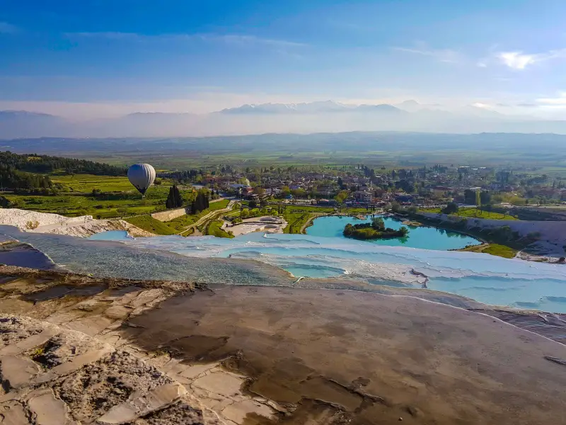 Panoramic view of Pamukkale village, the travertine terraces, and a hot air balloon